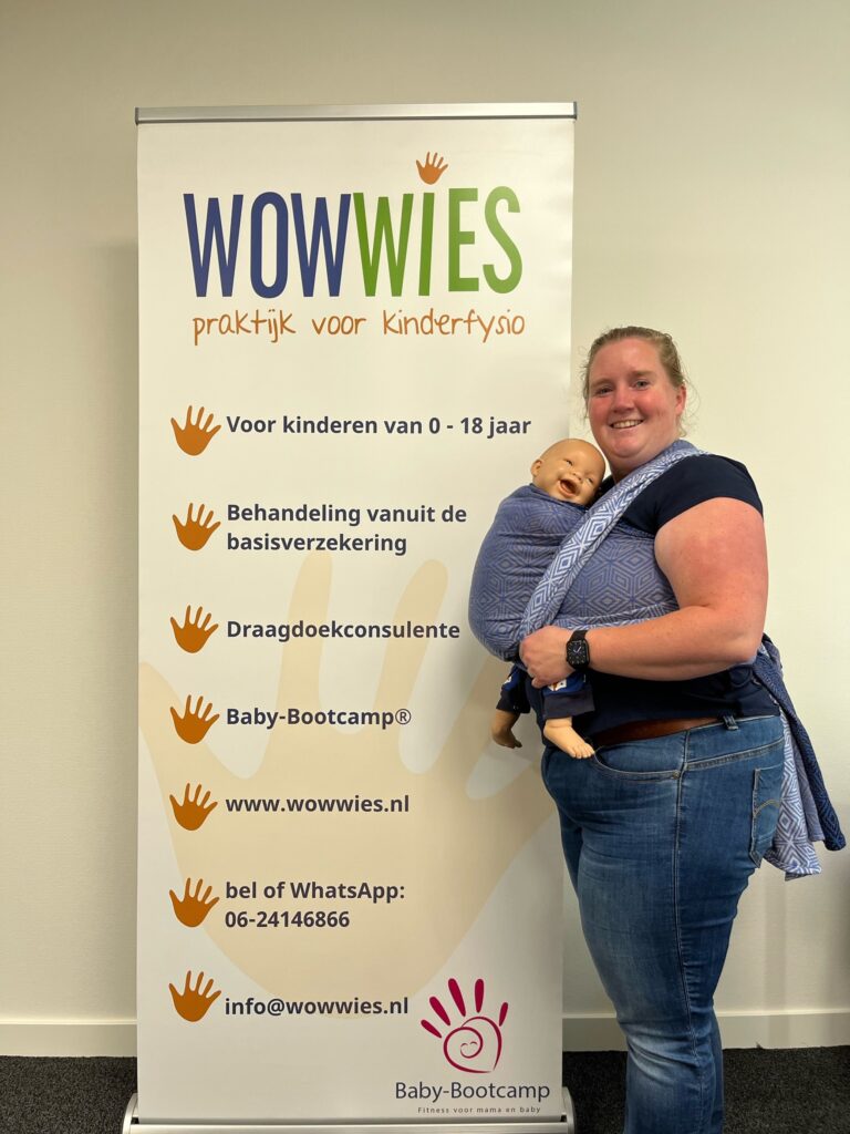 WowWies met draagdoek om met draagpop erin bij haar banner met informatie over WowWies erop